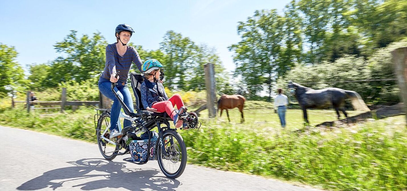 Frau und Kind fahren auf einen Tandem Rad und an einer Pferdewiese vorbei 